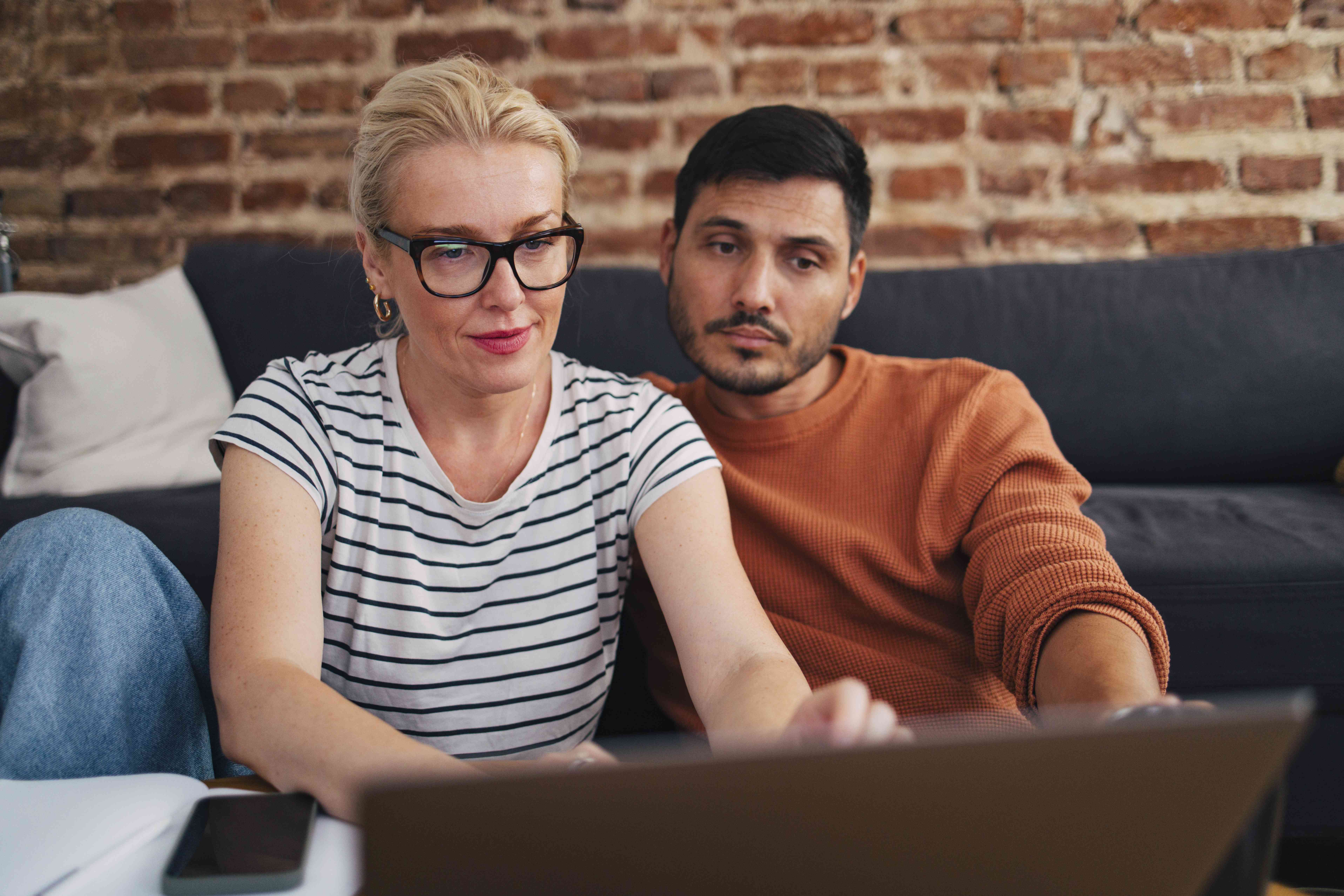 Couple in their 30s sitting in their living room and looking together at a laptop