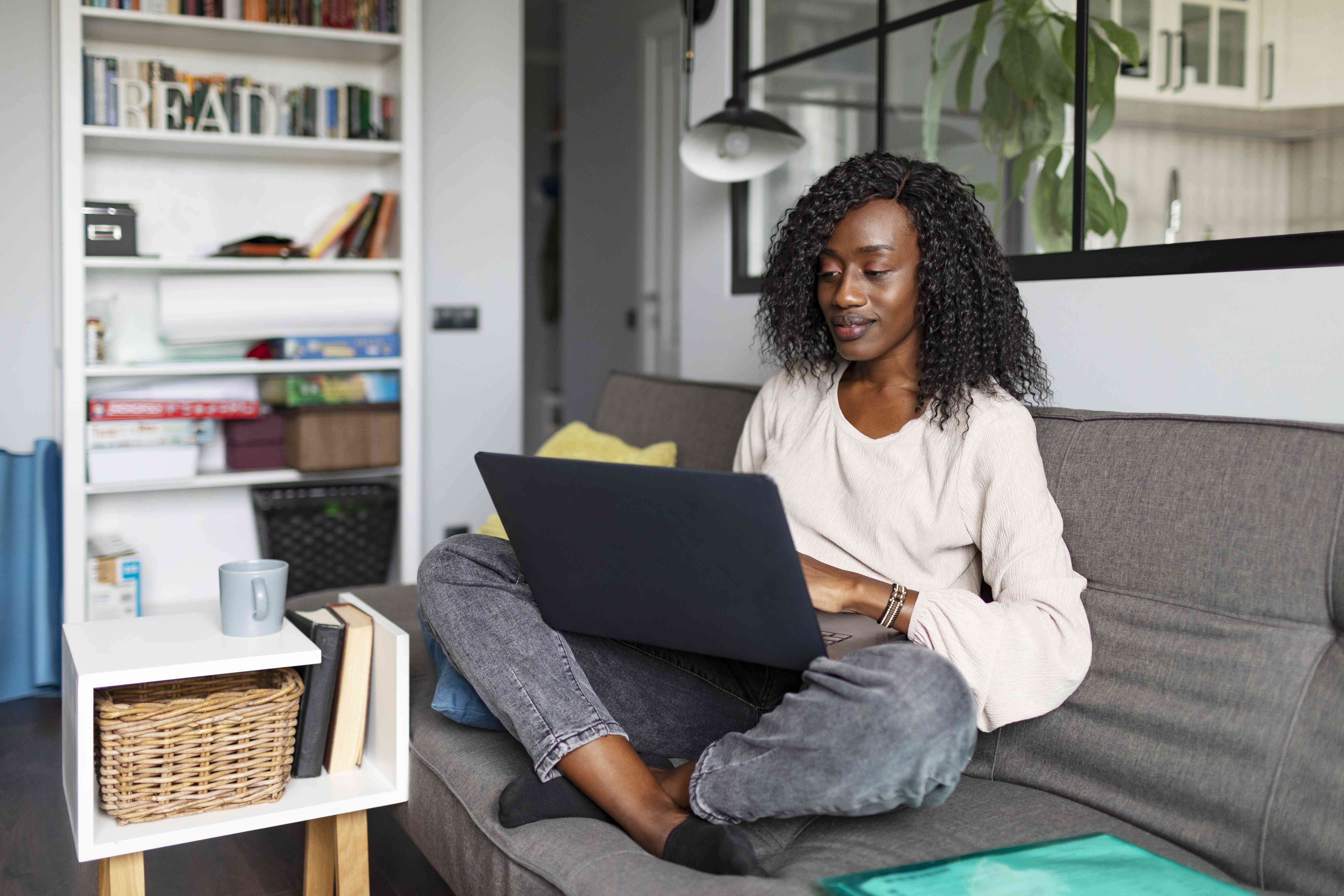 A woman sits on a couch with her legs crossed looking at a laptop