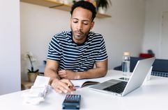 Man doing paperwork with a calculator and laptop