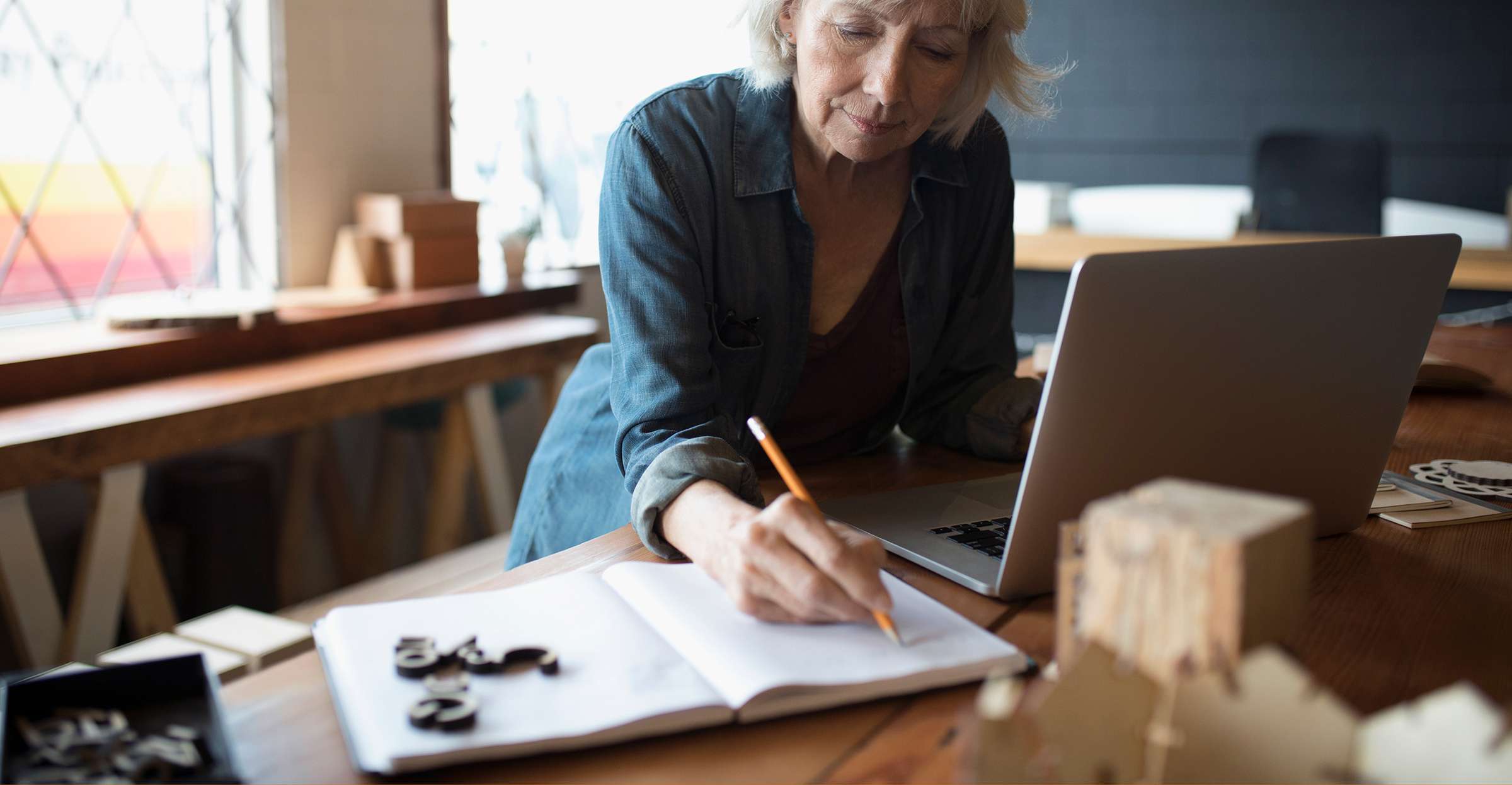 A mature woman makes notes with a notebook and laptop as she plans for retirement. 