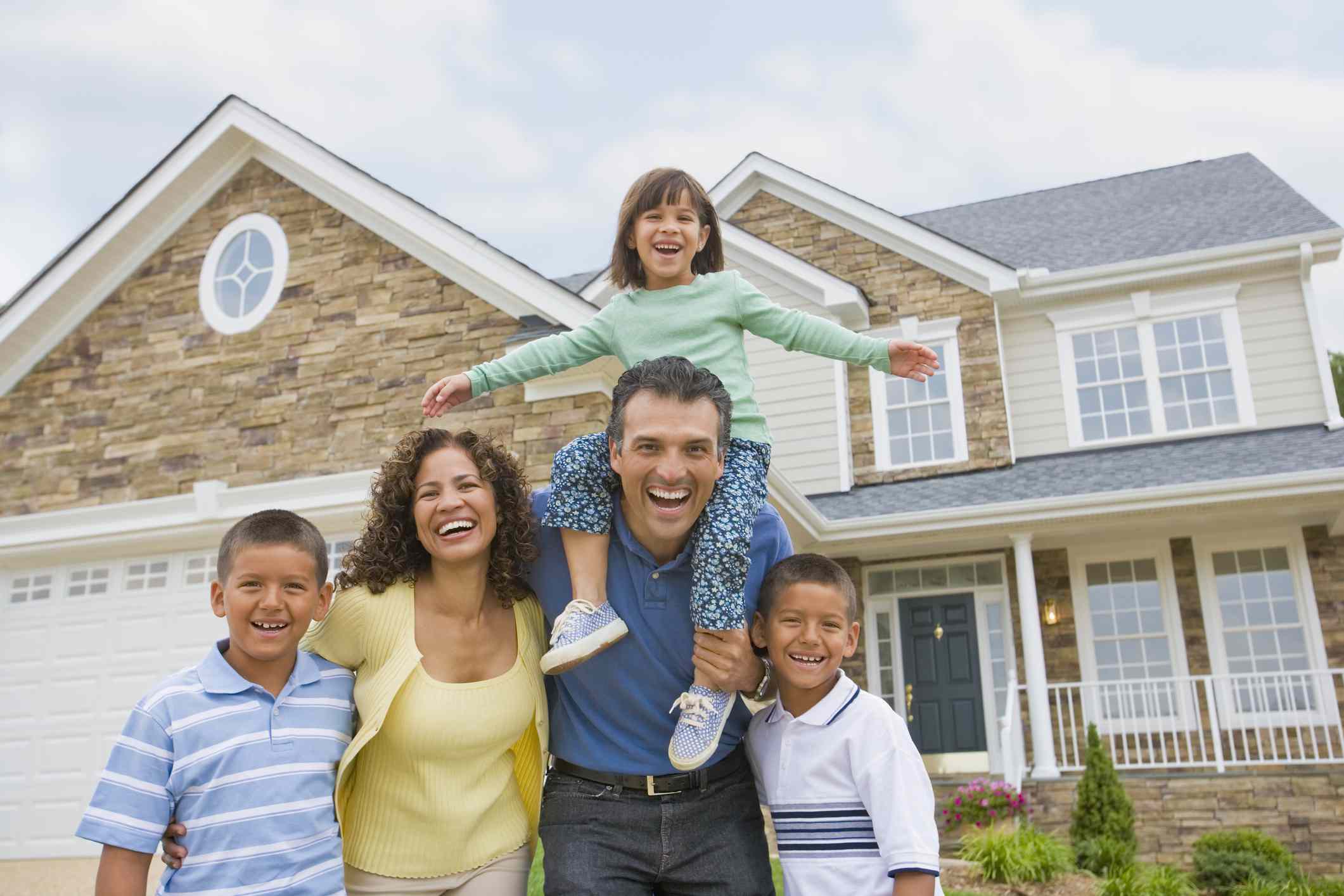 Family of five smiling in front of a house