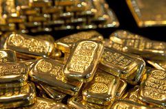 A closeup of gold bullion bars laying in a pile on a surface. 