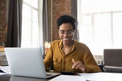 bespectacled smiling woman using the calculator and laptop