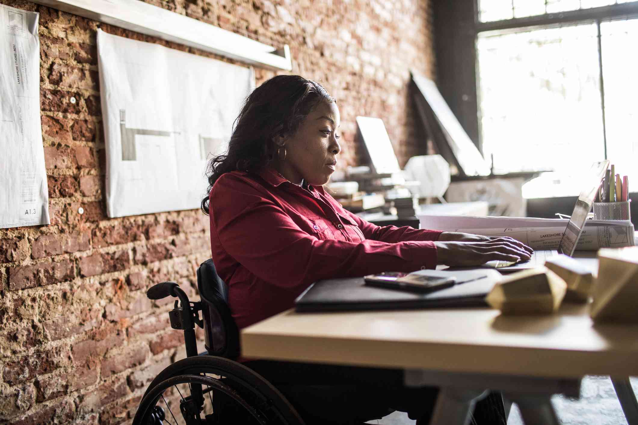 Someone in a wheelchair working at a desk in an office, using a laptop computer.