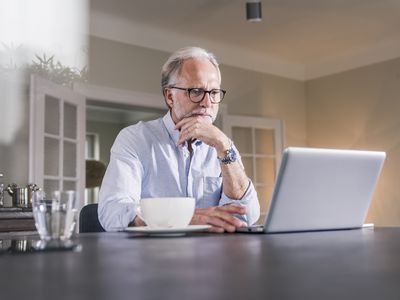 Older man sitting at his dining room table and looking intently at his laptop screen