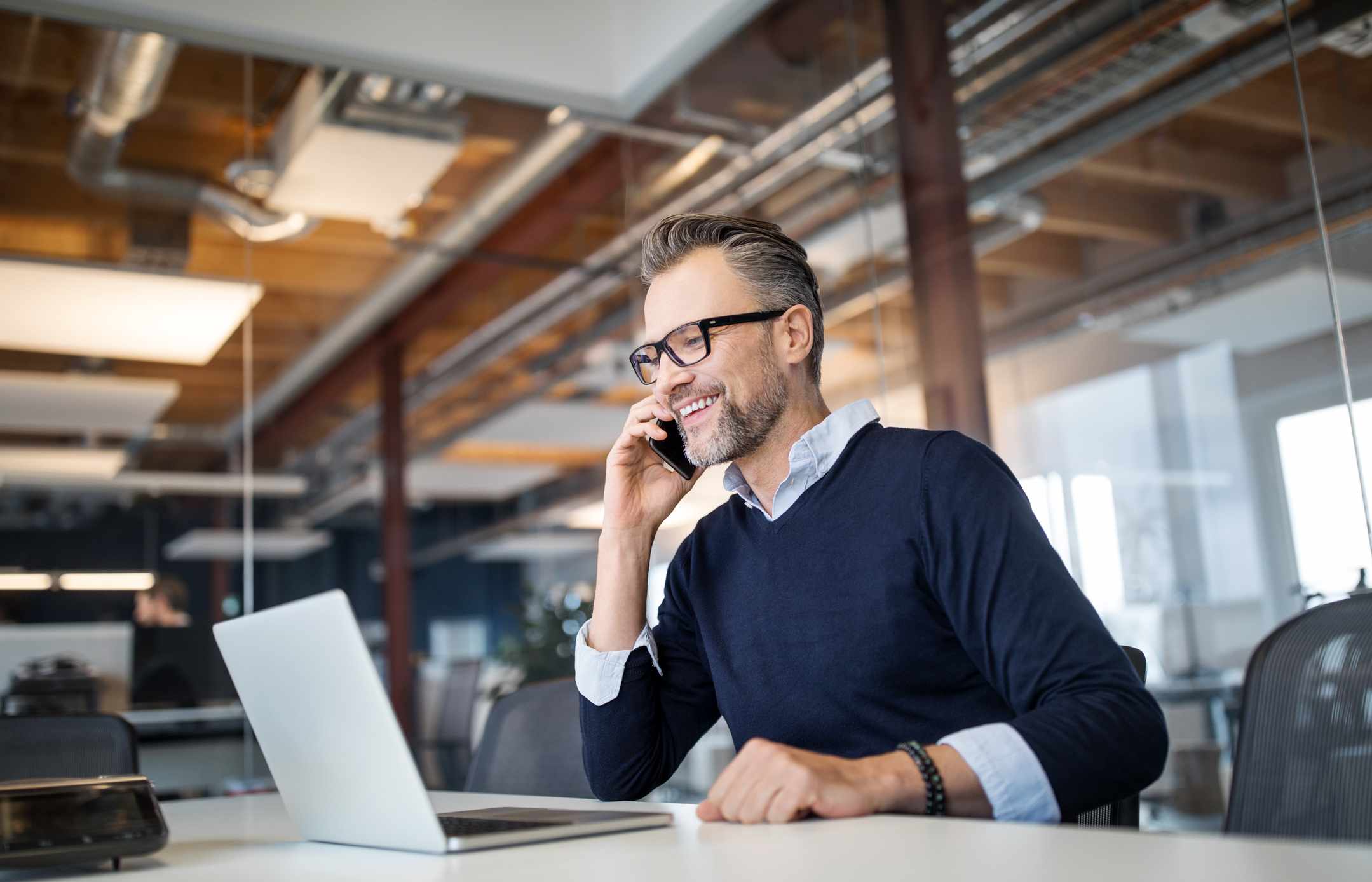 Professional in a modern office on his phone while looking at his laptop