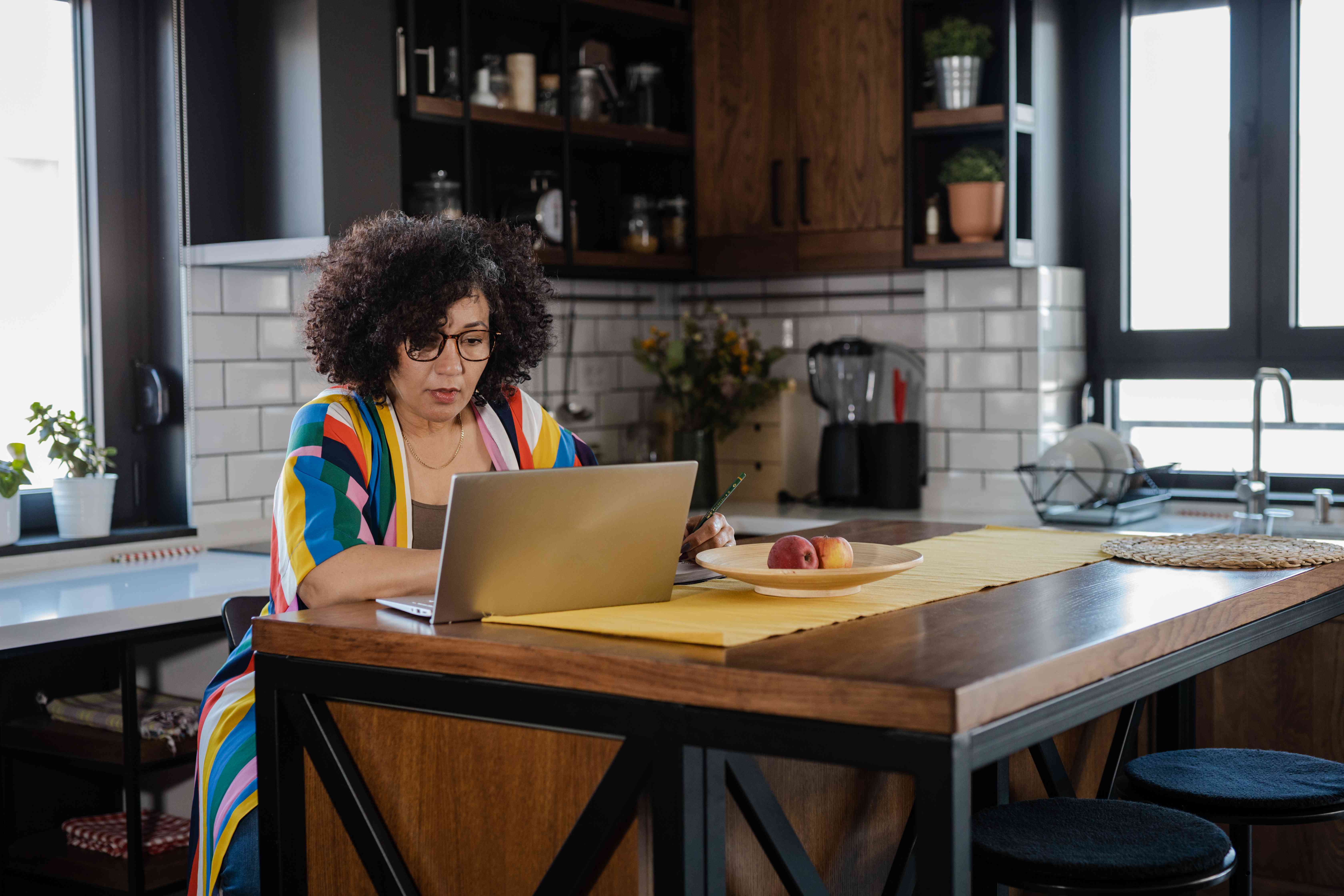 A woman in a colorful sweater sits at a kitchen island with a laptop