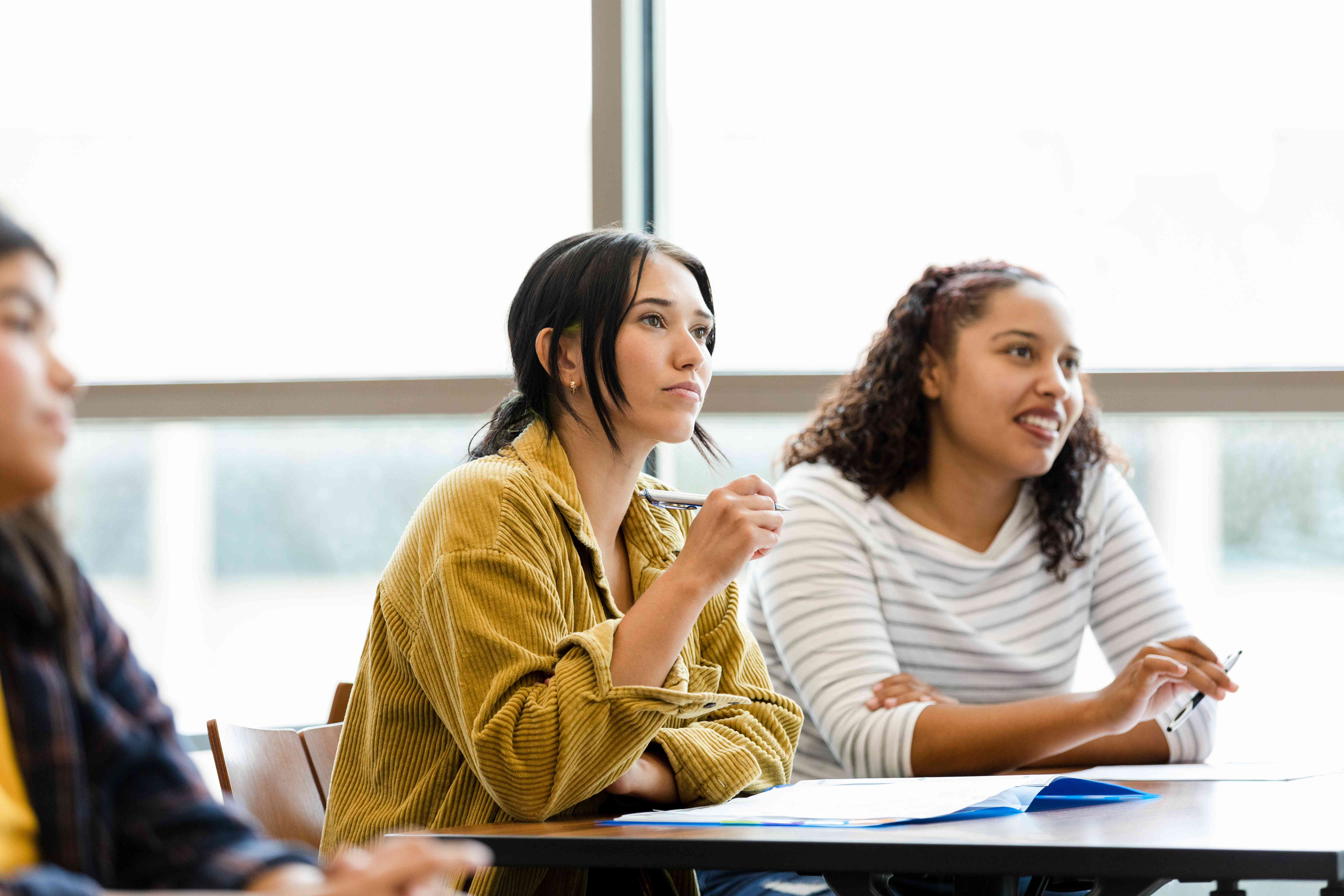 Two students sit at a desk in a classroom and listen to a lecture about whether it’s better to consolidate student loans.