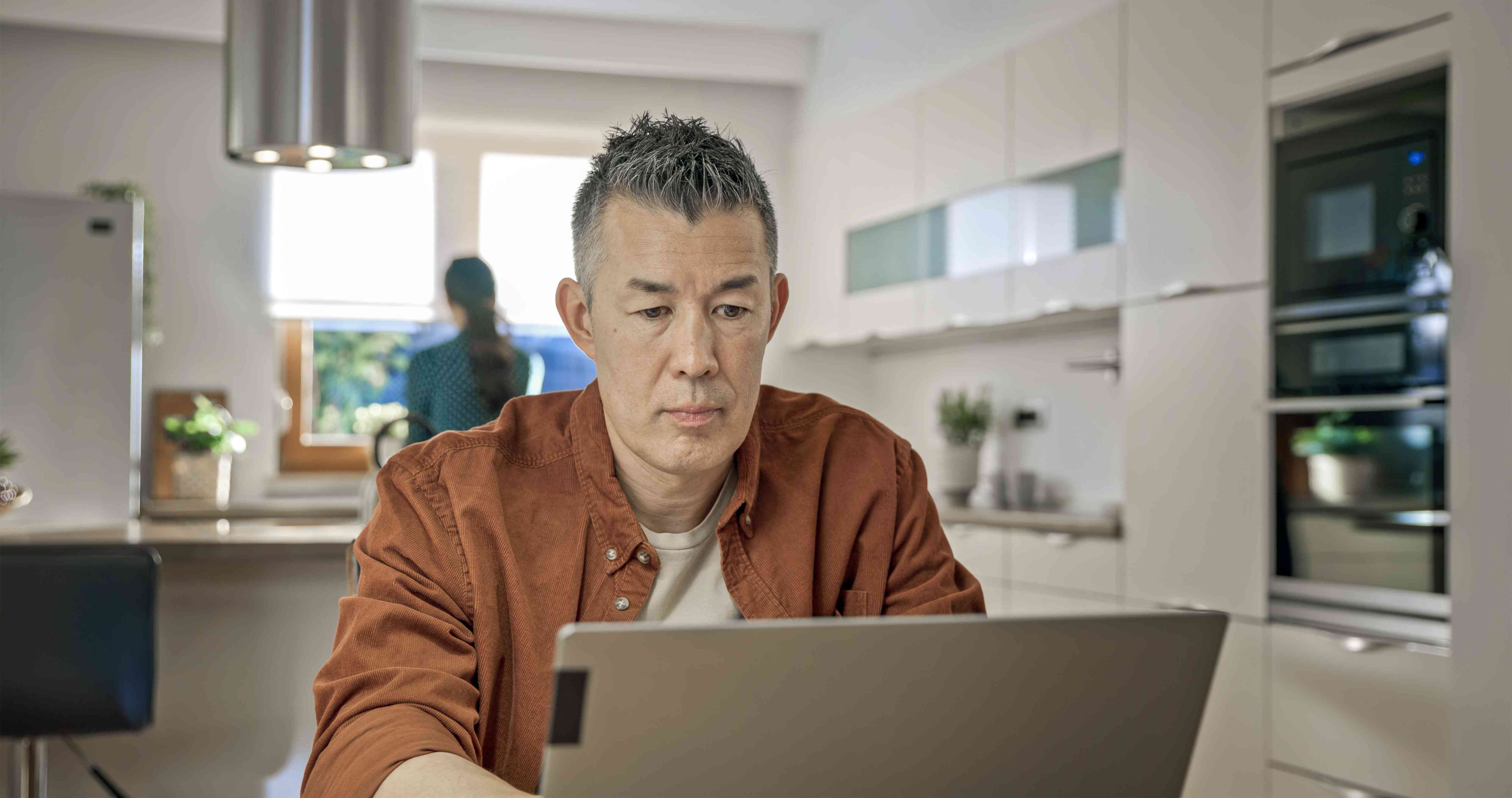 Older man sitting at his kitchen table while looking at a laptop