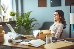 Woman sitting in modern office with book, computer, and boxes around her