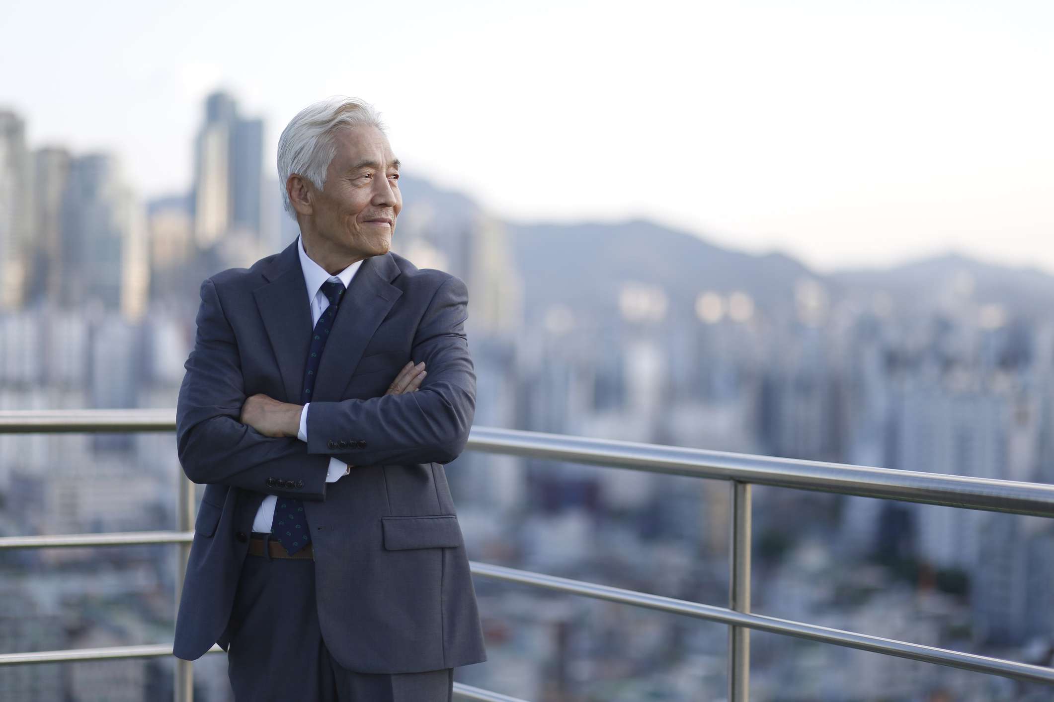 Senior businessman standing with arms crossed on a rooftop with a city skyline behind him