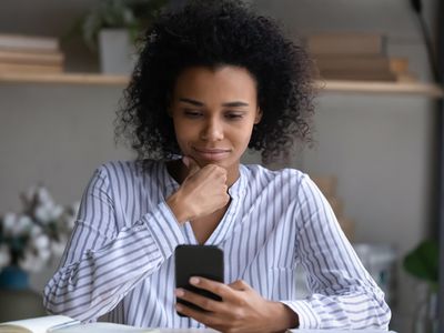 Young woman at home, pondering something on her smartphone with a slight smile