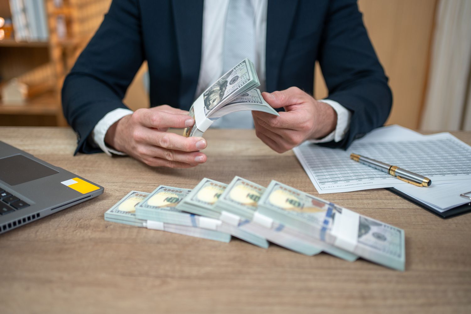 A person sits at a desk dividing large sums of money into smaller stacks for eventually deposit into different bank accounts to avoid detection from police.