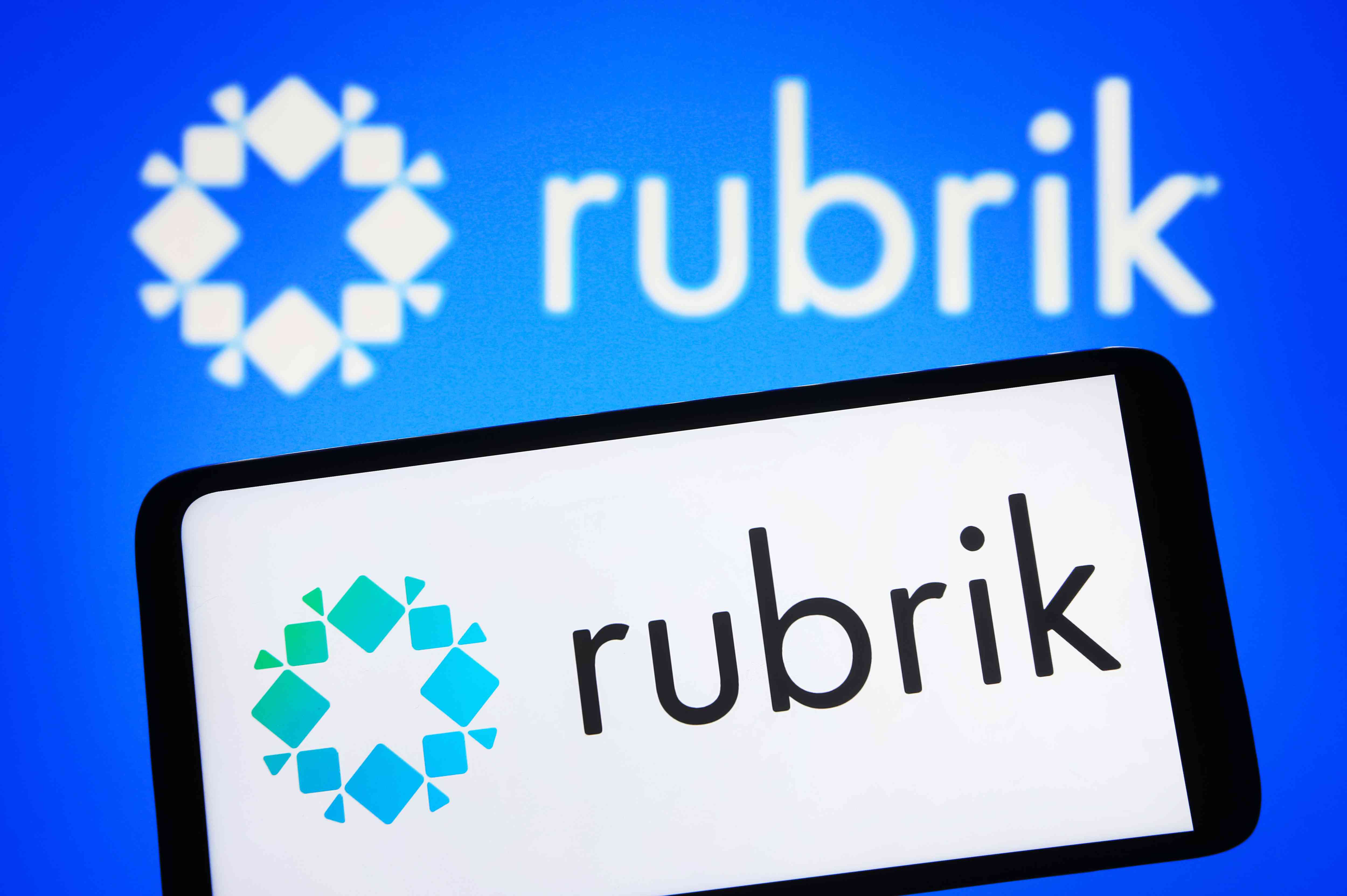 Rubrik logo is seen on a smartphone and on a PC screen