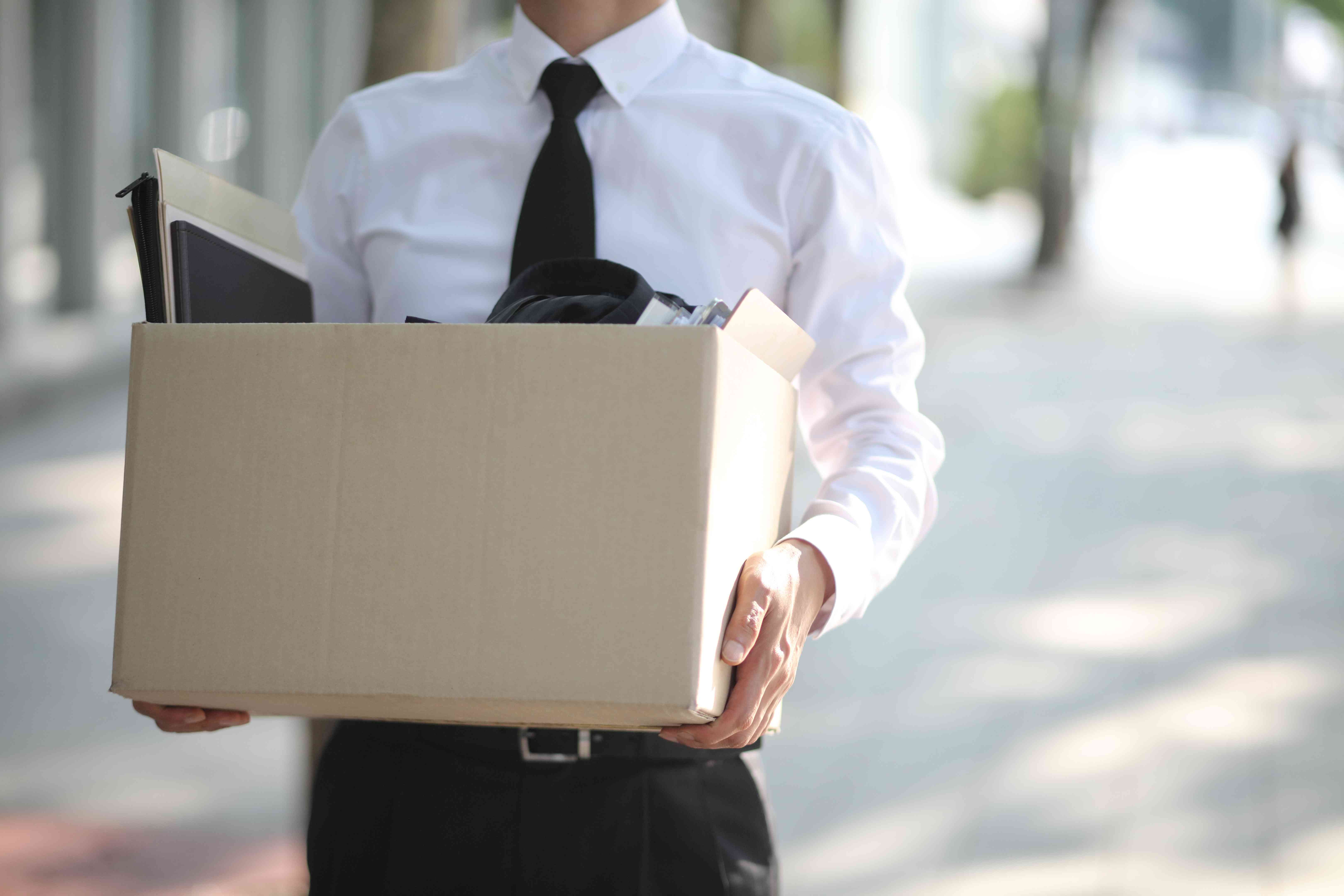 Man in a white shirt with a black tie holding a box full of papers