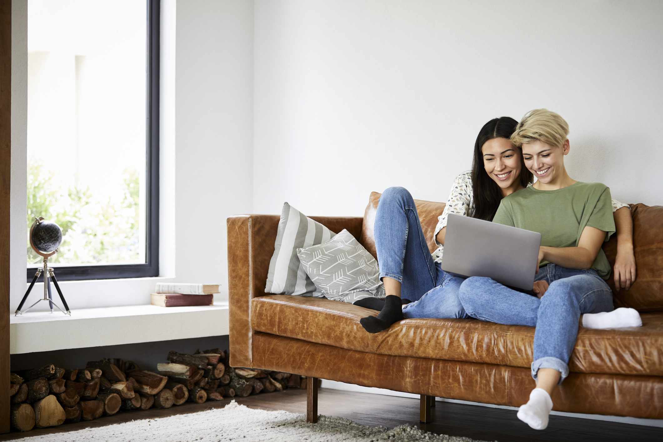 Smiling couple watching movie on laptop. Young woman is spending leisure time with girlfriend. They are sitting on sofa at home.