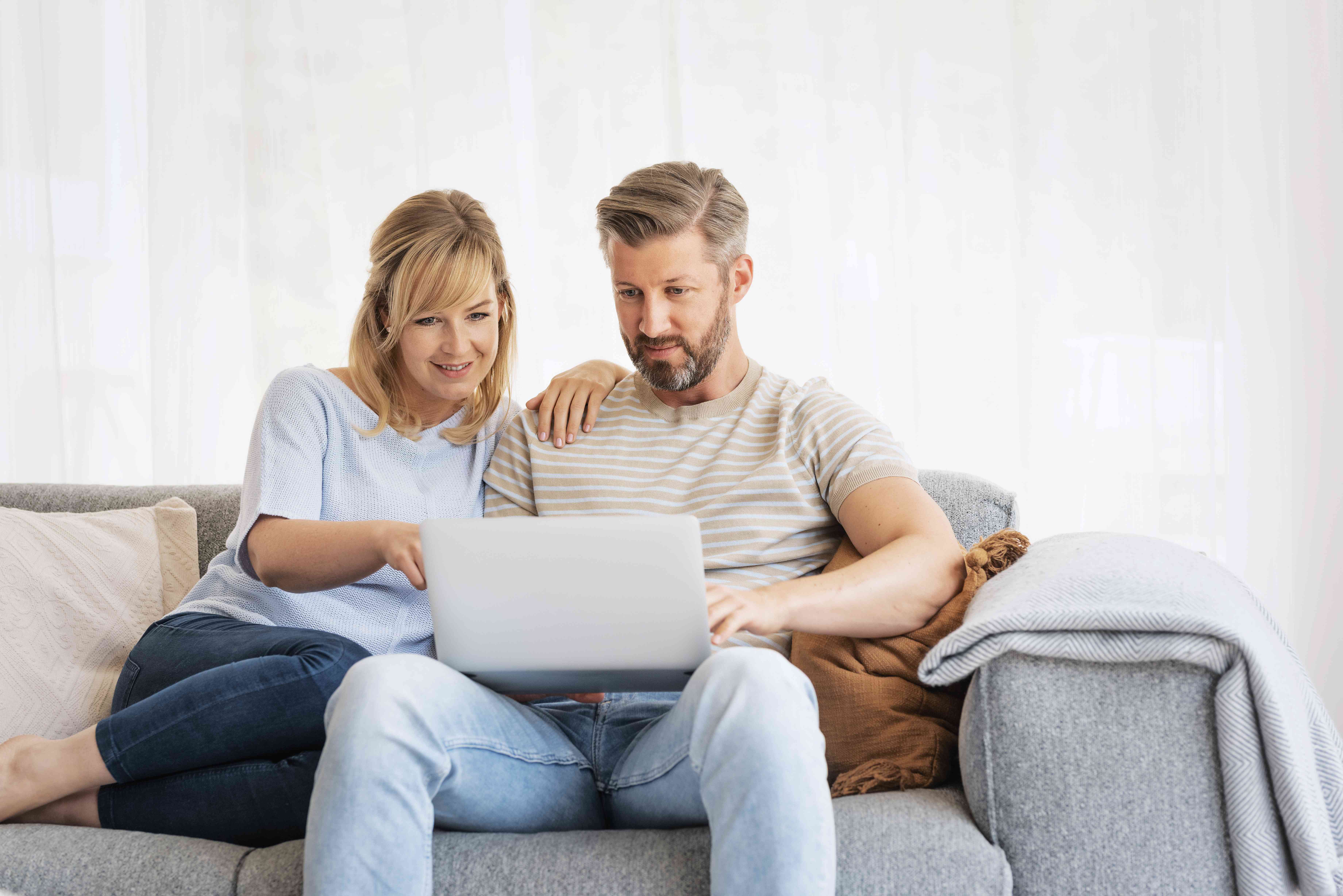 Couple in their 40s sitting together on their living room couch and looking at a laptop screen