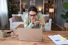 Confused person sitting at home in the living room trying to identify debit card fraud.