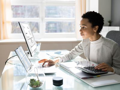 Young professional Black woman checking finances on a laptop while sitting at a desk. 