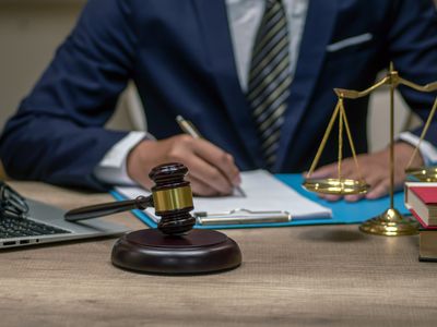 Businessperson in a suit with a gavel and mini-scale of justice nearby.