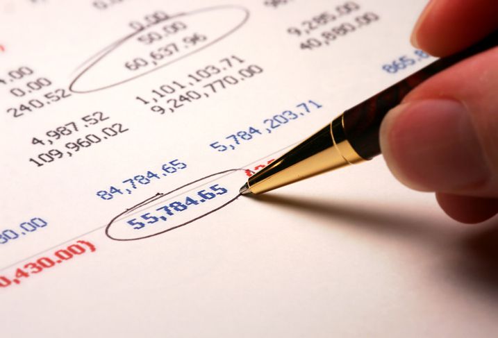 Cropped photo of a balance sheet containing numbers with some circled by a pen being held by someone