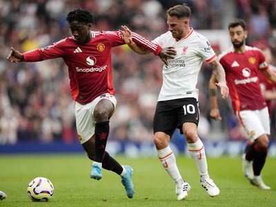 A Manchester United player dribbles a soccer ball away from a Liverpool player.