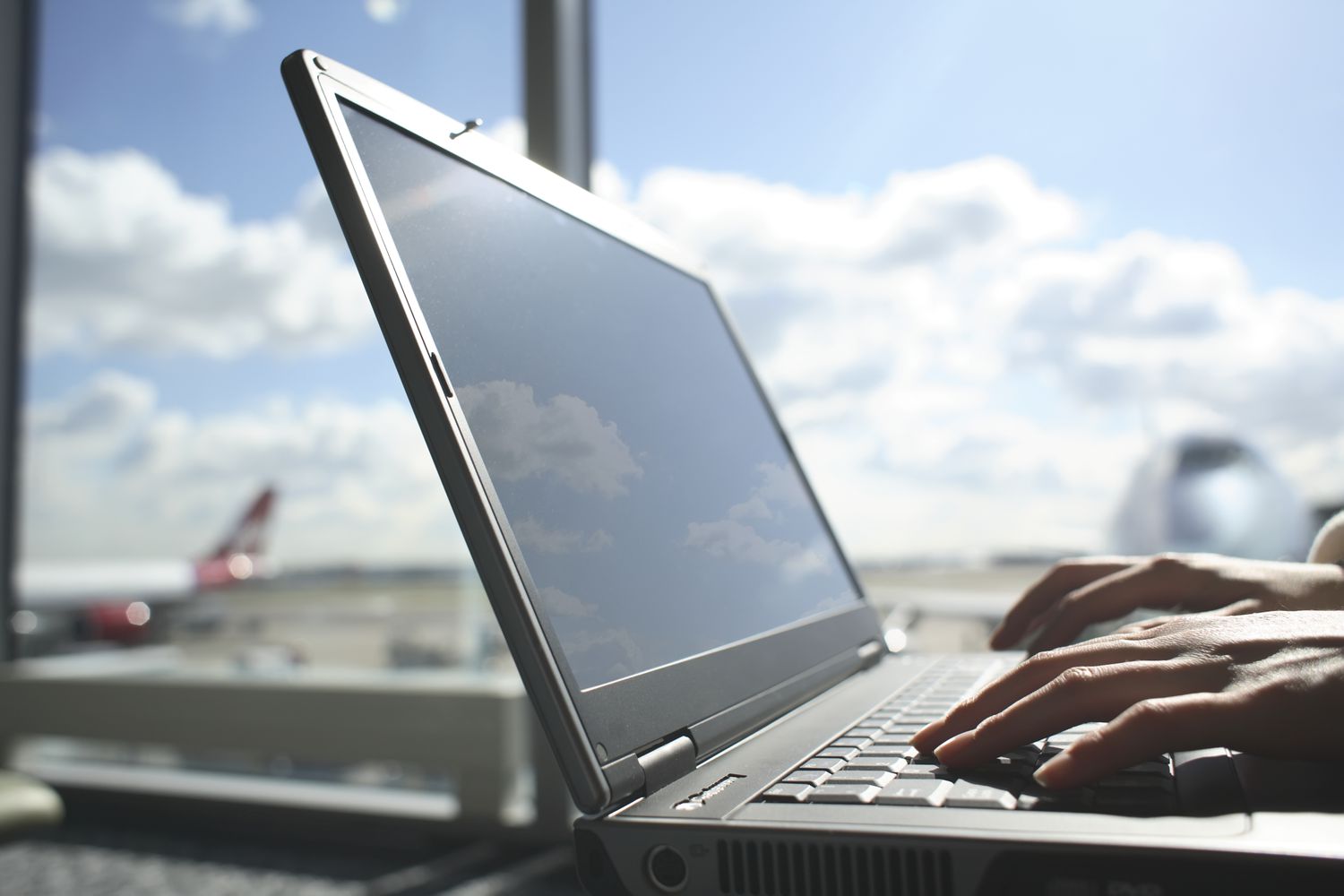 Hands on a laptop keyboard with an airport in the distance.