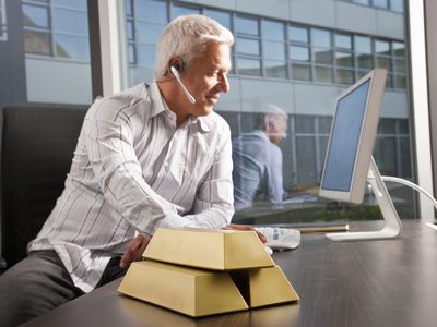 An investor looks at a computer screen with three gold bars in the foreground. 