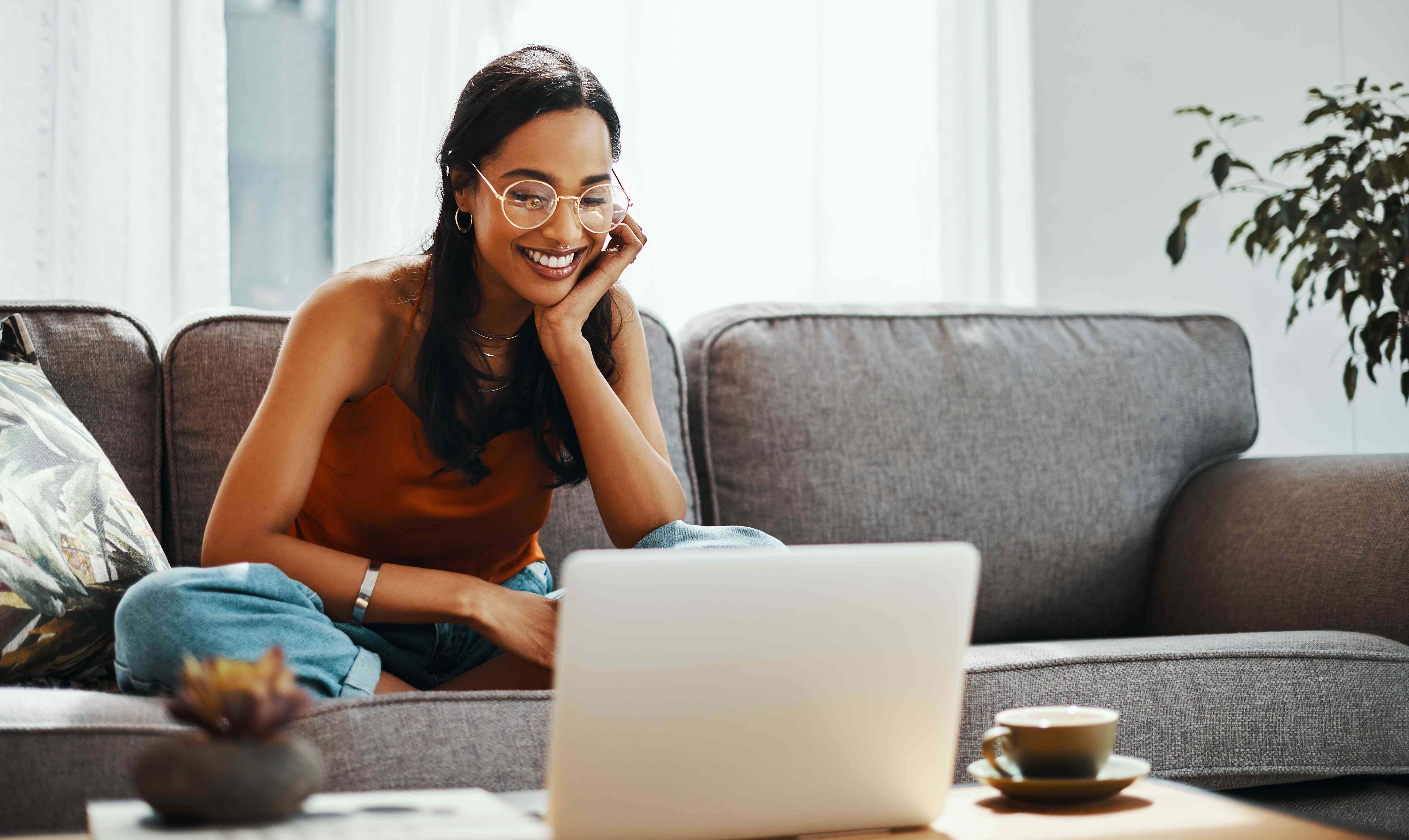 A young woman shops for a car online, smiling at a laptop while sitting on a couch.