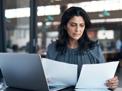 An investor sits at a desk with printed documents in their hands as they review the difference between investing in a Roth IRA account and a Traditional IRA account.