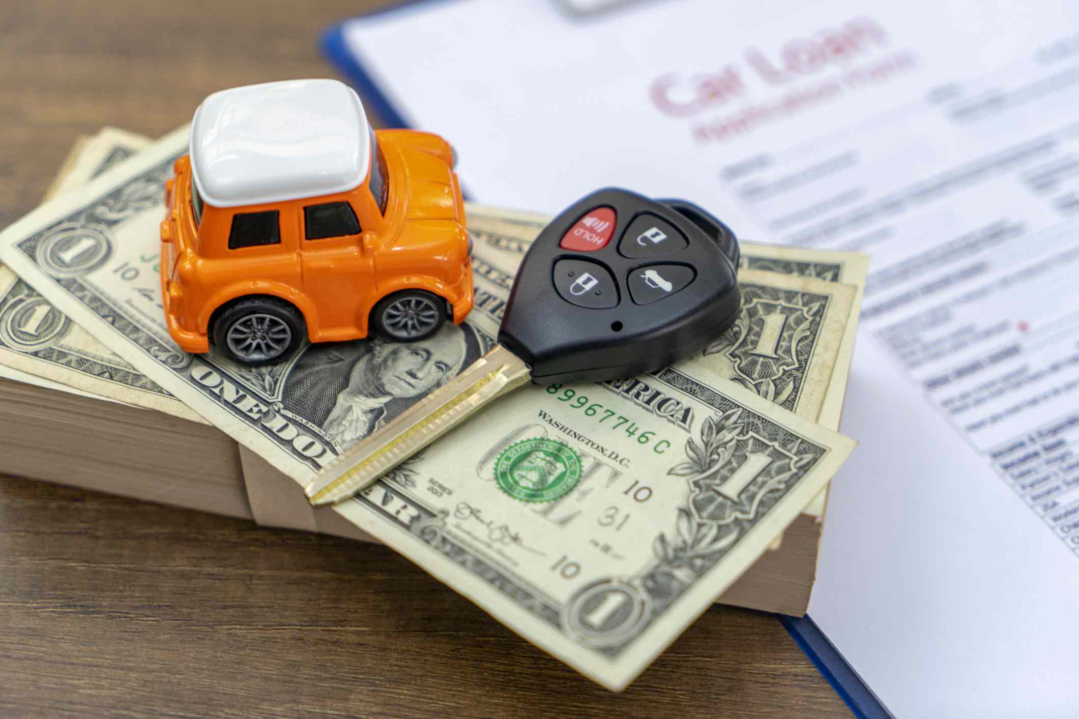 Stack of money with car keys and a toy keychain next to car loan paperwork