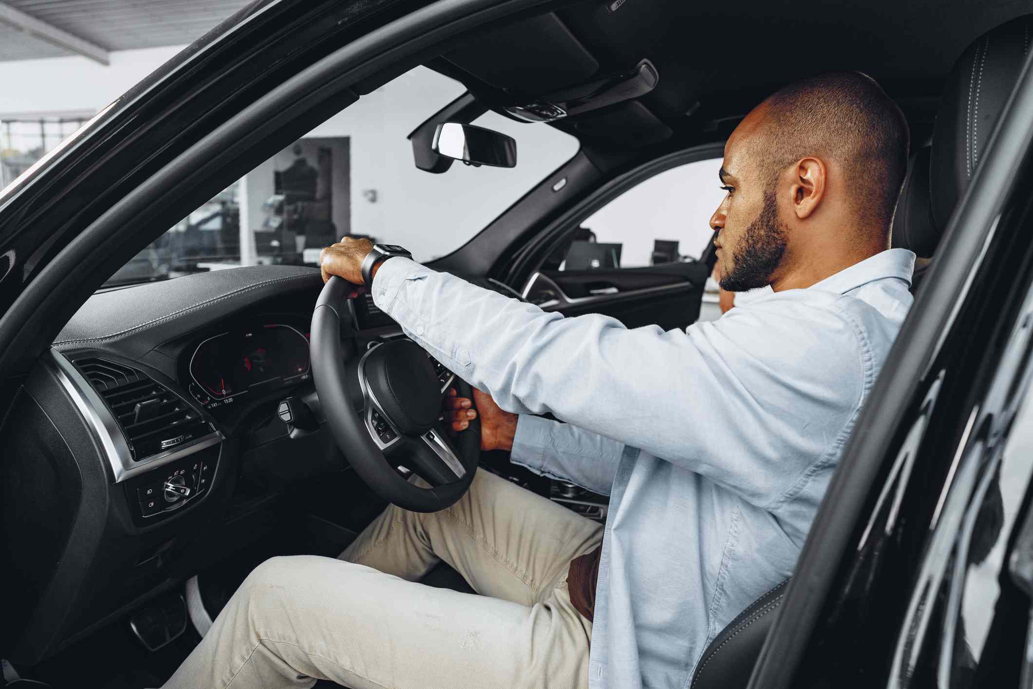 Young Black man sitting in a new car in car showroom and looking around