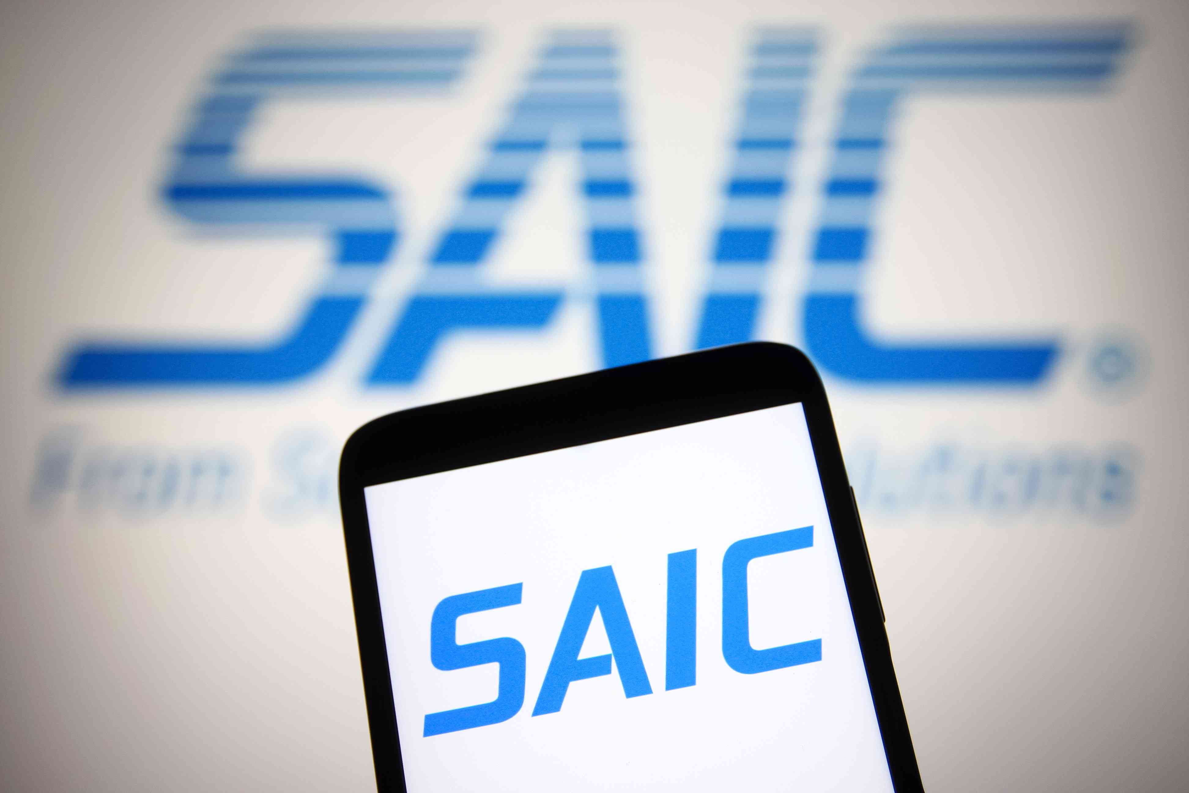 A SAIC (Science Applications International Corporation) logo is seen on a smartphone and a PC screen