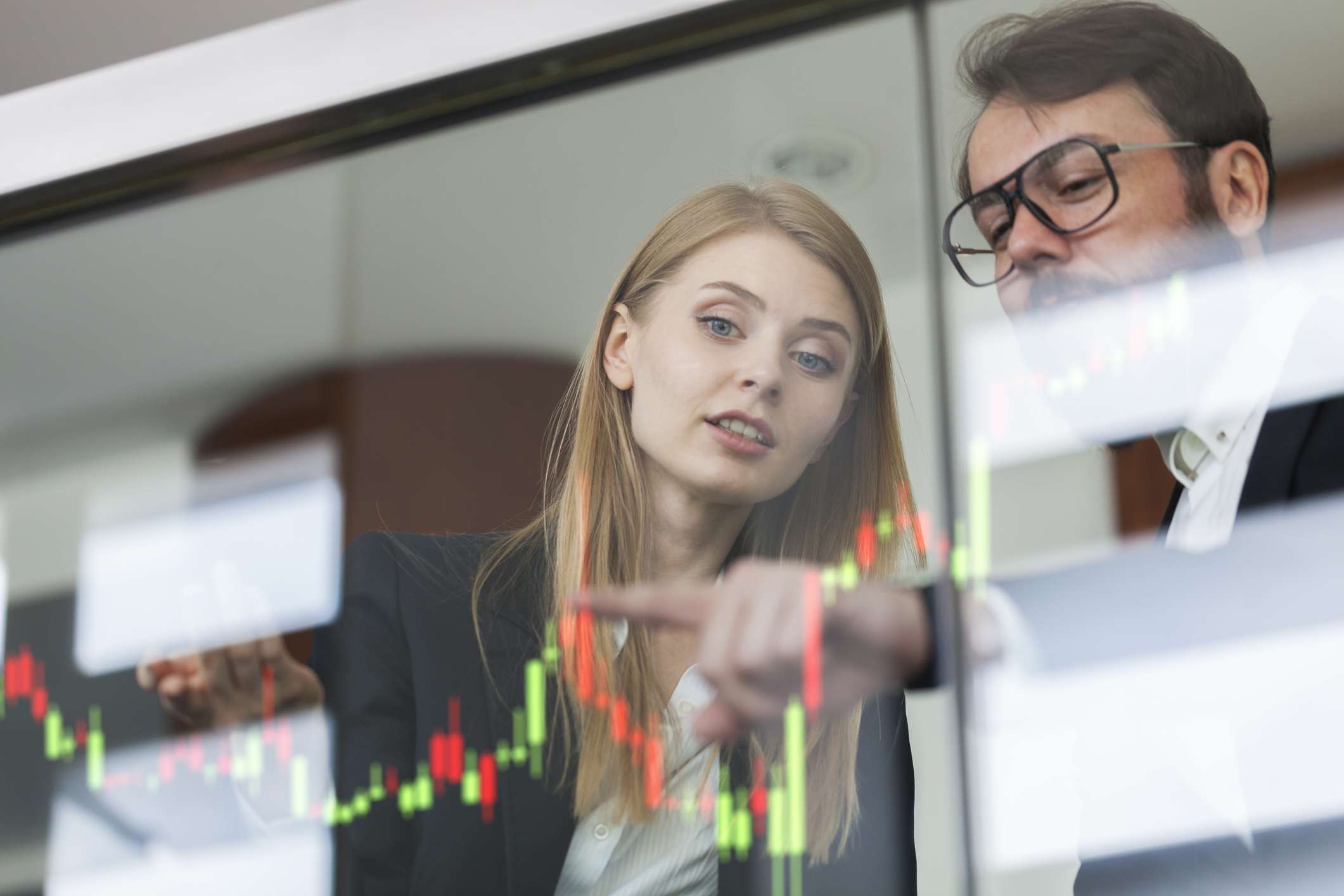 Businesswoman and businessman talking and pointing to stock chart on a clear wall display