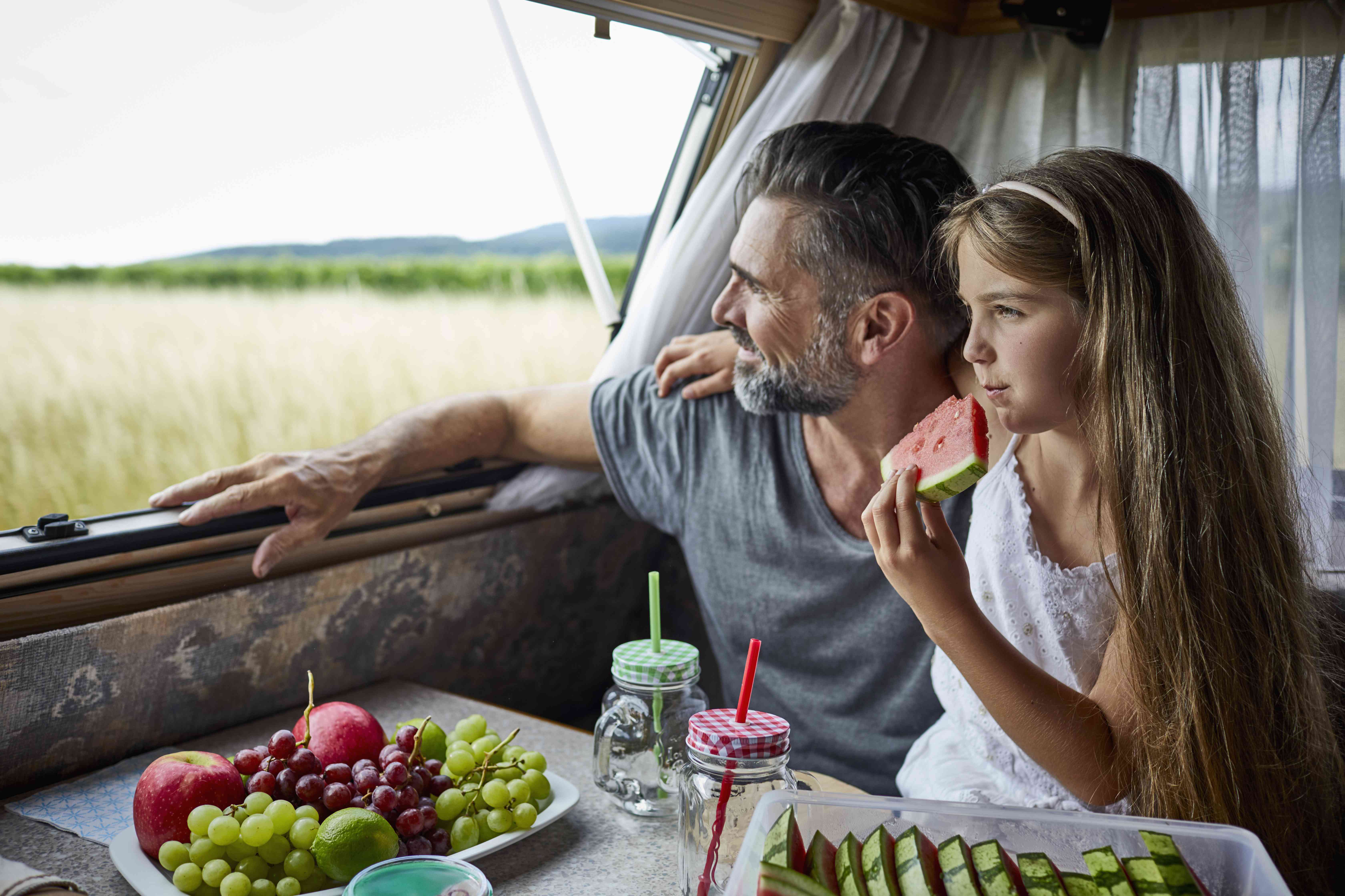 A man and a young girl eat fruit in an RV.