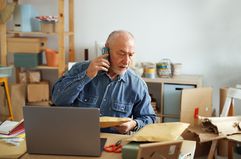 Investor sitting at a desk with an open laptop and talking on a cellphone