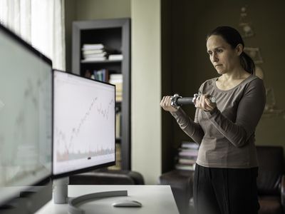 Female trader working at home, standing in front of two monitors and exercising.