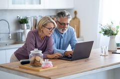 A mature couple looking at a laptop computer together in a kitchen