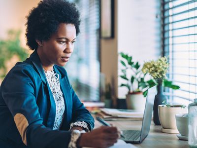 Woman holding a pen and looking at a laptop