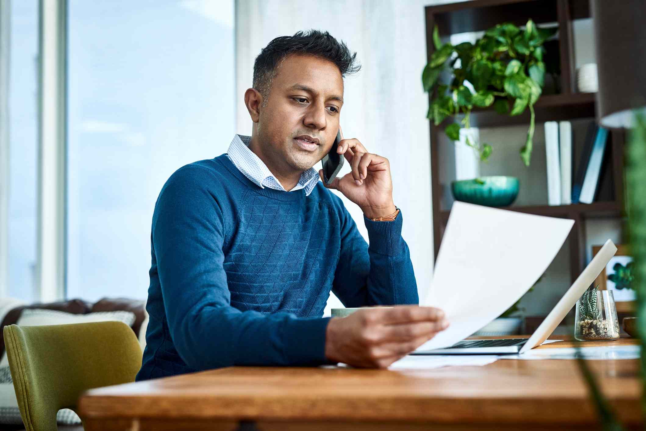 A man talks on the phone while holding documents.