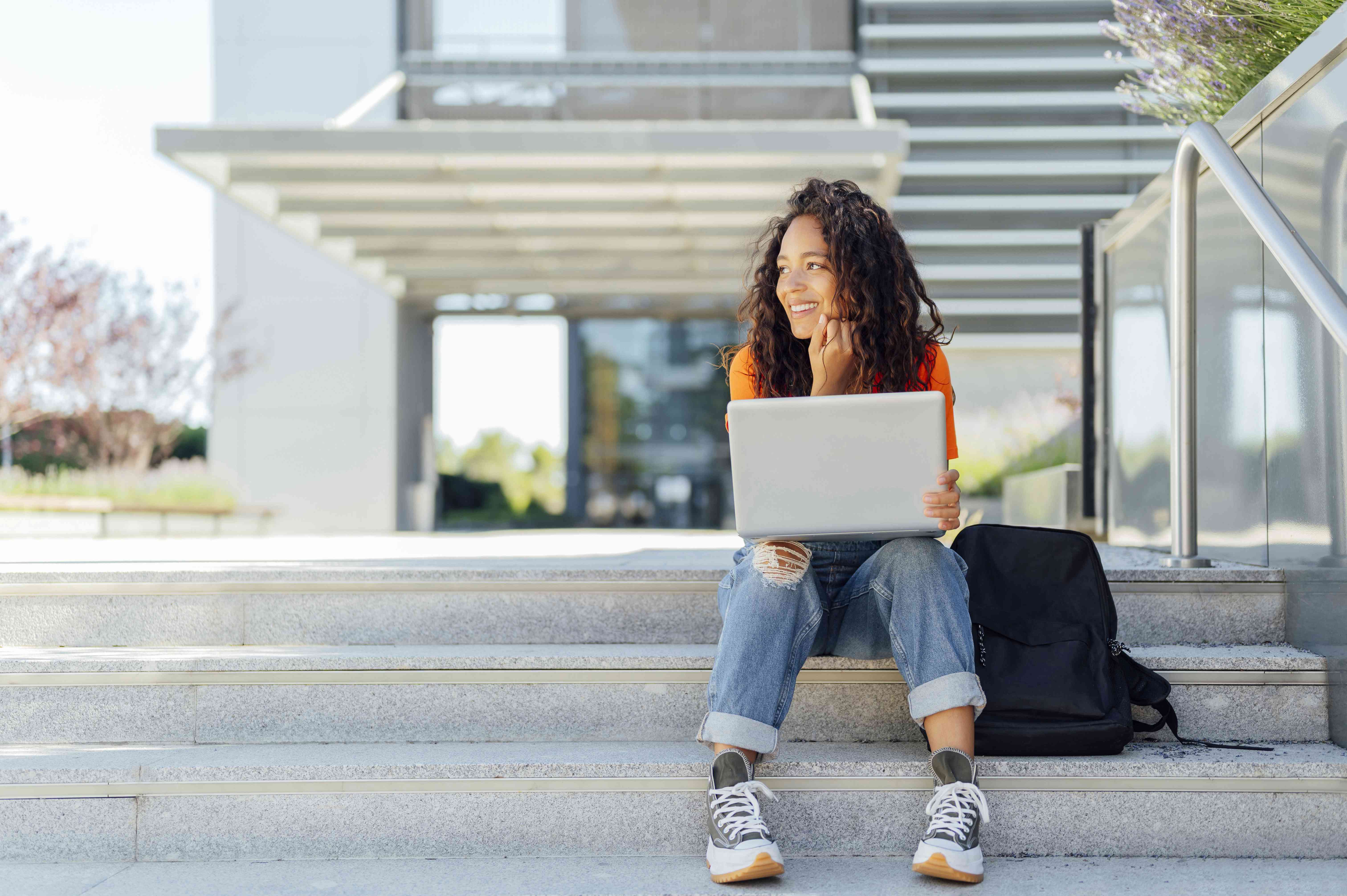 A student sits on the steps of a campus researching how a student loan is different from a scholarship.