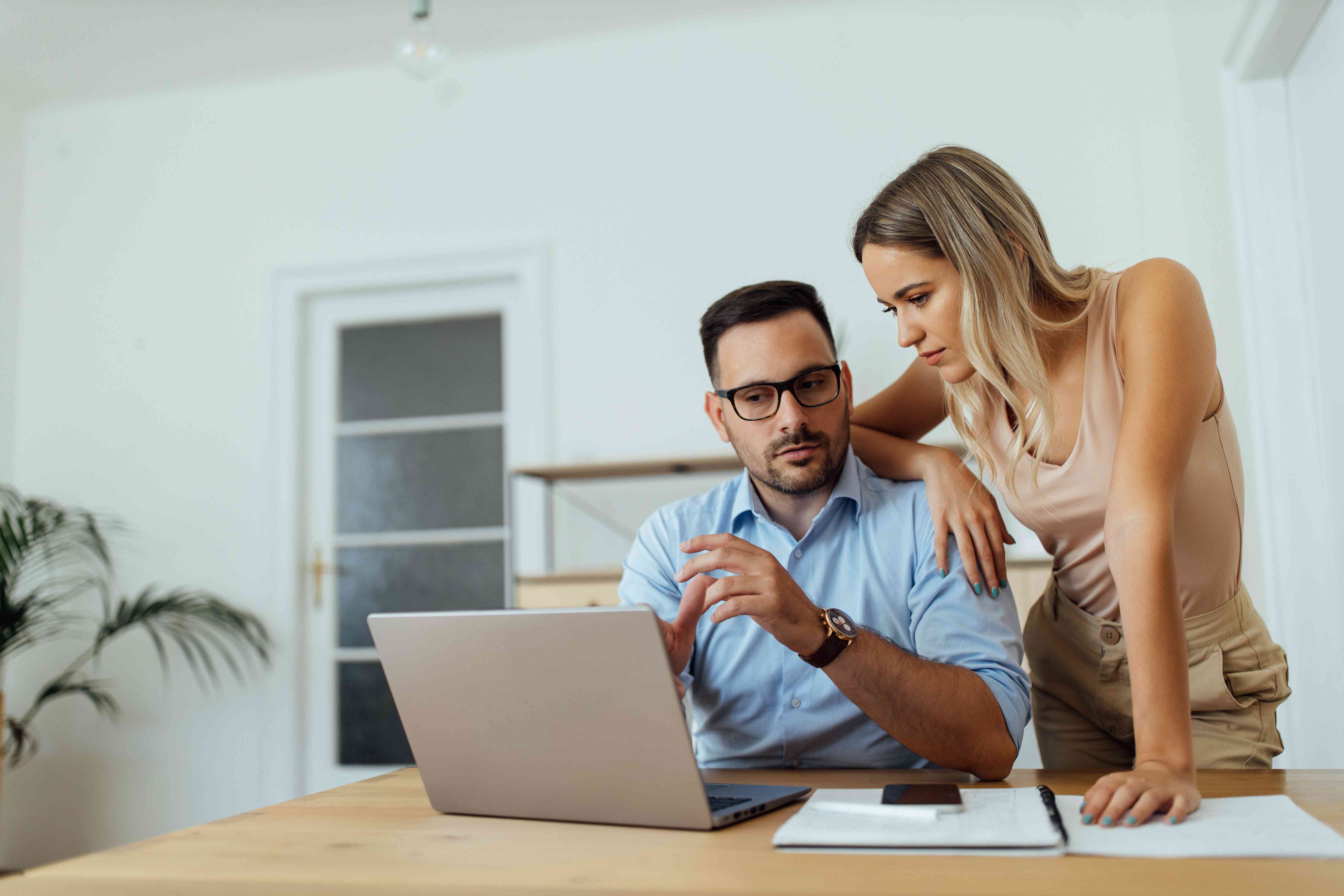 Couple in their late 20s or early 30s together at home, contemplating something they see on a laptop screen