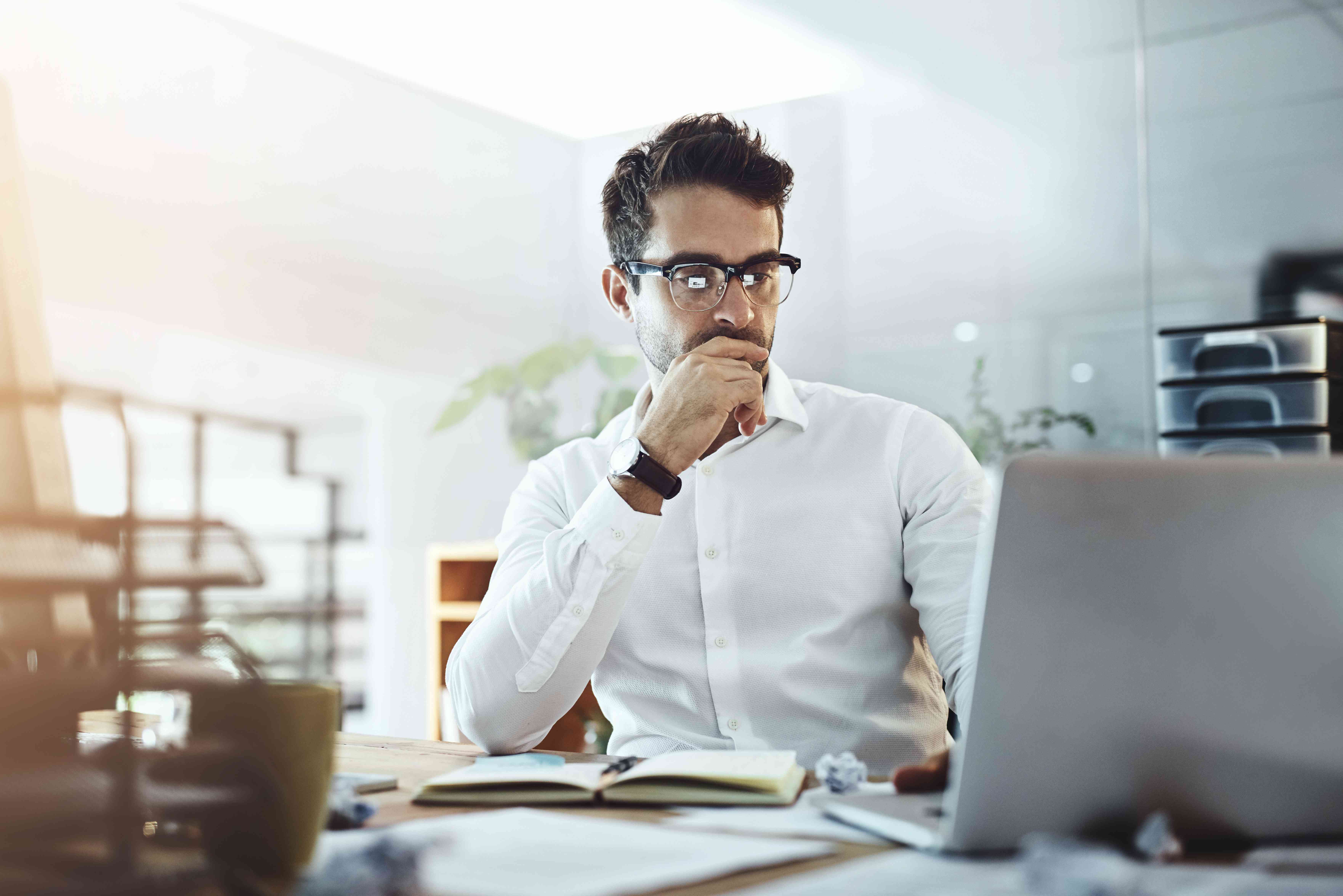 Man in his 30s at his home office desk, looking seriously at his laptop screen