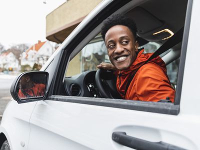 Smiling young driver looking back through window while driving delivery van