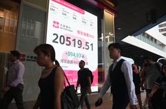 Pedestrians walk past a sign showing the numbers of the Hang Seng Index in Hong Kong.