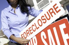 A woman puts a “Foreclosure” sign over a “For Sale” sign in front of a house