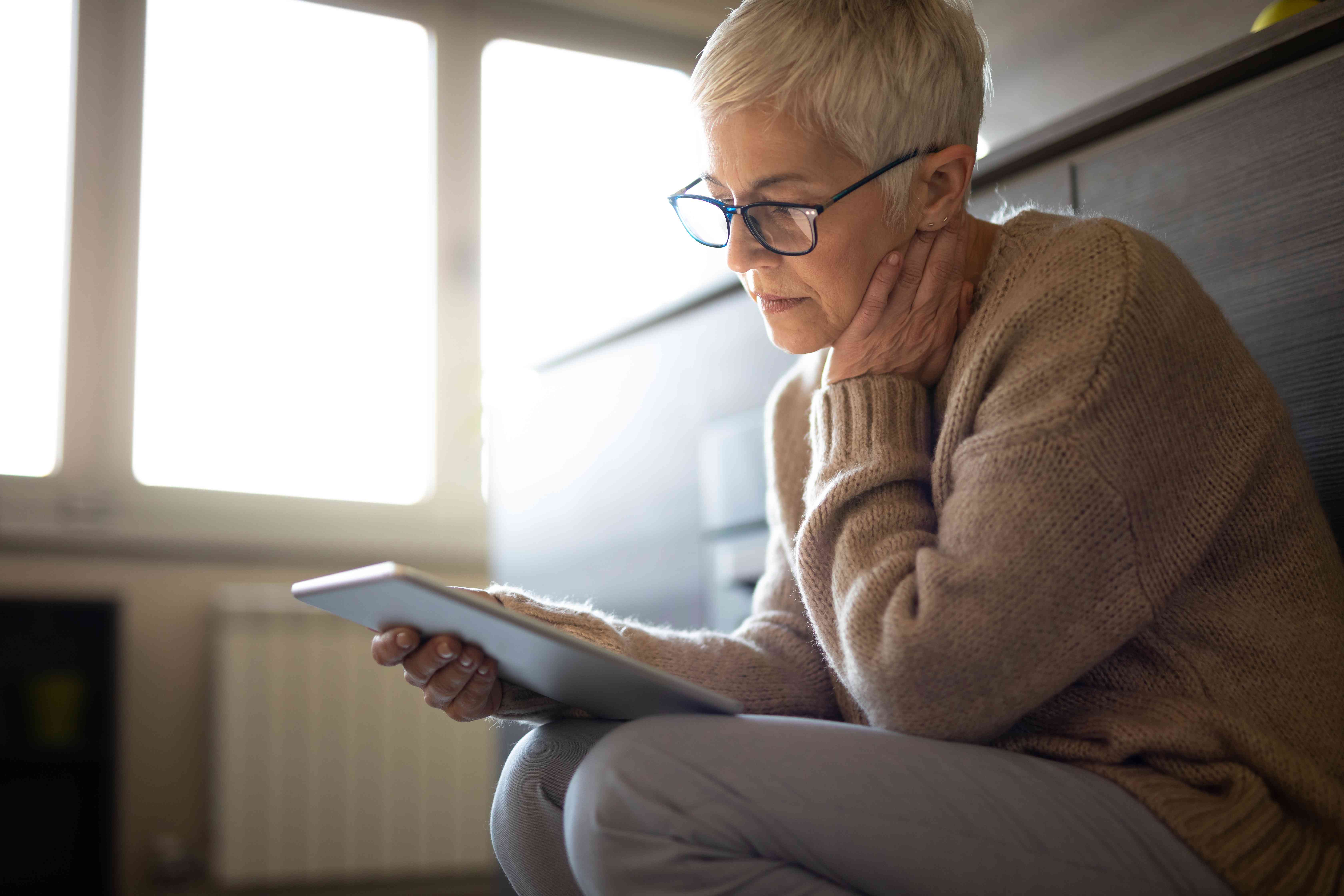 Older woman sitting at home and looking very seriously at something on her tablet