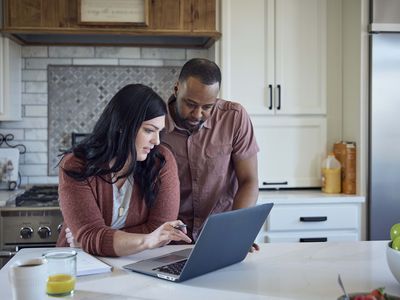 woman and man sit at kitchen counter working on laptop