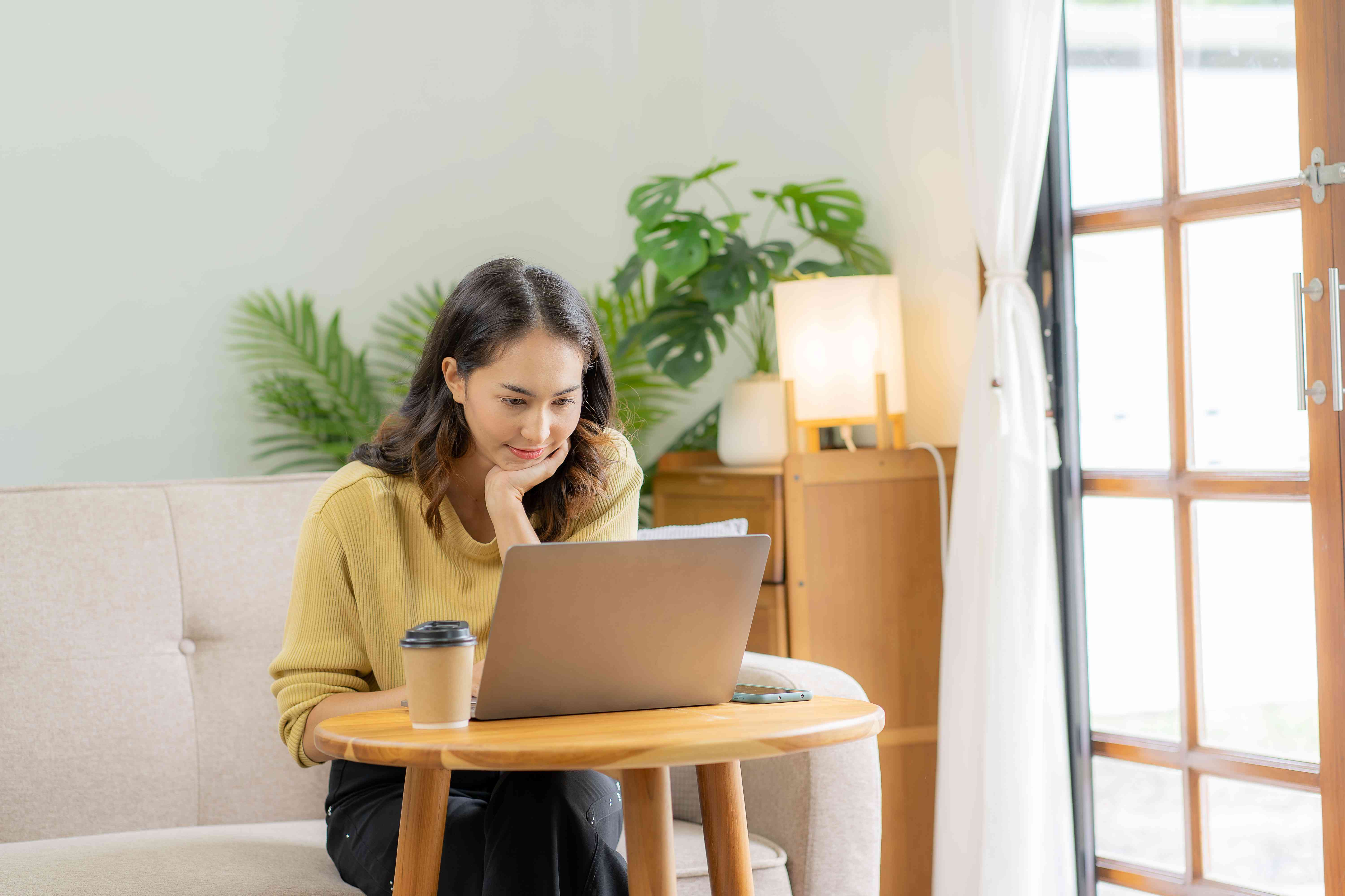 Young woman sitting on couch and looking at her laptop with a smile on her face