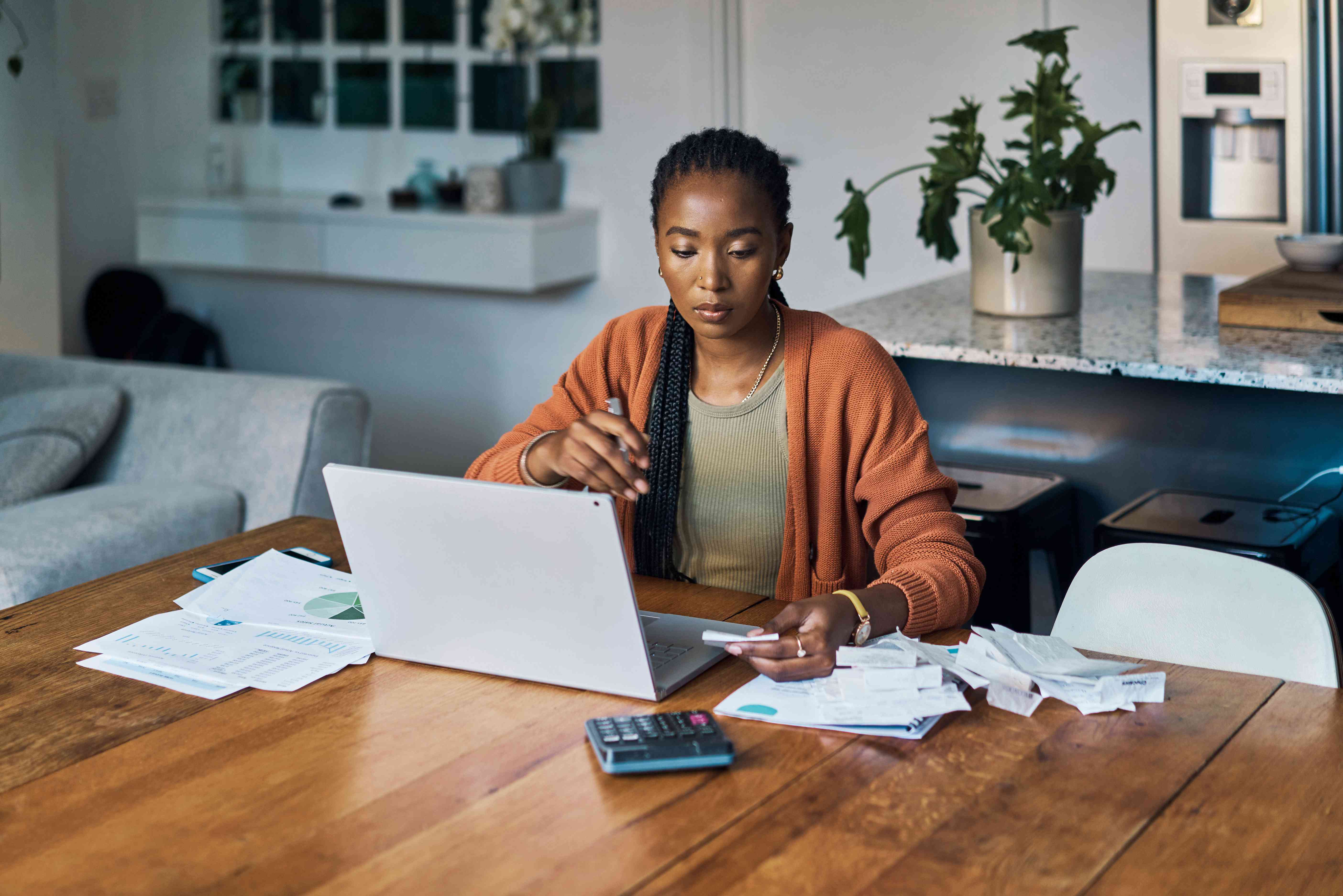 A woman reviews papers and works on a laptop at a table.